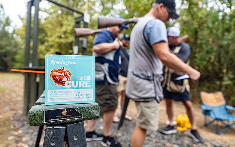 Gun Club Cure box sitting on a ledge with shooters in the background