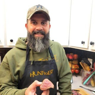 John Wallace standing in a kitchen holding a piece of meat