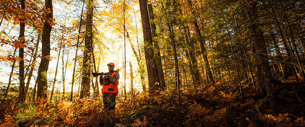 hunter standing in a wooded area with a rifle on his shoulder