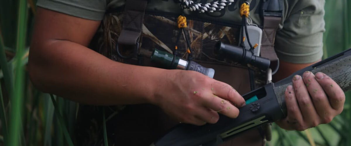 hunter kneeling behind a falling tree with his rifle leaned against it