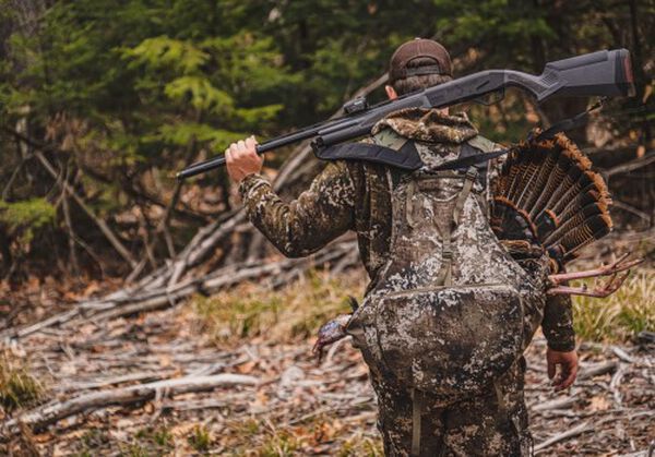 Hunter carrying a rifle on their back and a dead turkey in their backpack