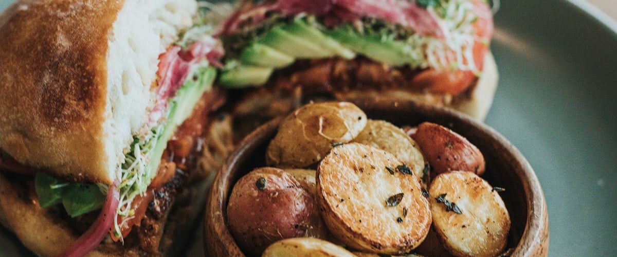 turkey sandwhich on a plate with a bowl of roasted potatoes