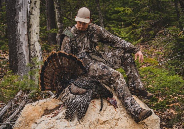 hunter sitting on a rock with a dead turkey