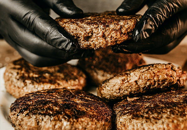 cooked burger being help in someones hands above a plate full of cooked burgers