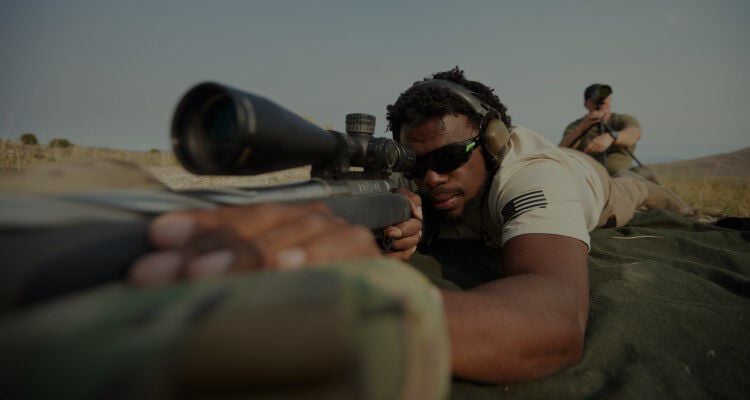 Man looking down the scope of a rifle while in a prone position