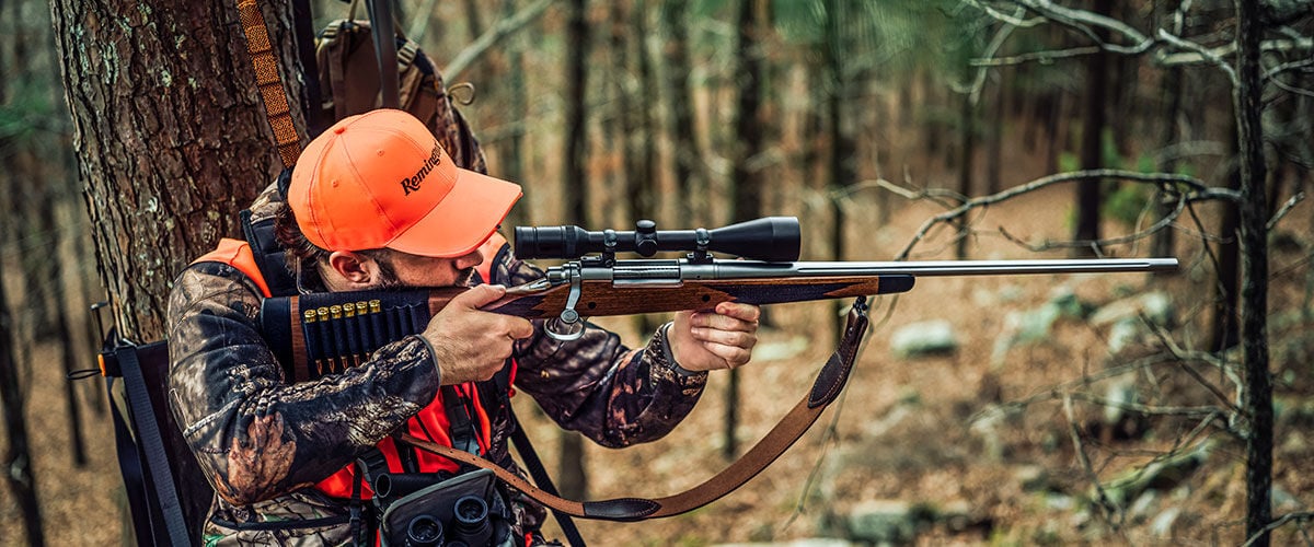 hunter sitting in a tree stand aiming a rifle