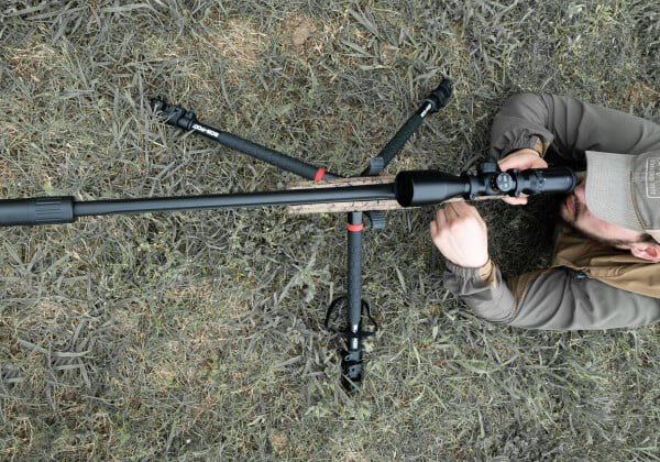 shooter looking down the scope of a rifle with a suppressor