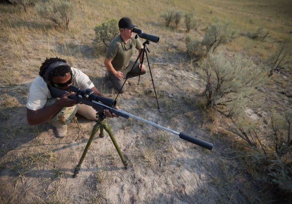 Long range shooter looking down a rifle scope next to a spotter