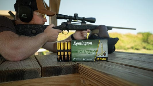 shooter aiming rifle at a range next to a box of Core-Lokt Tipped