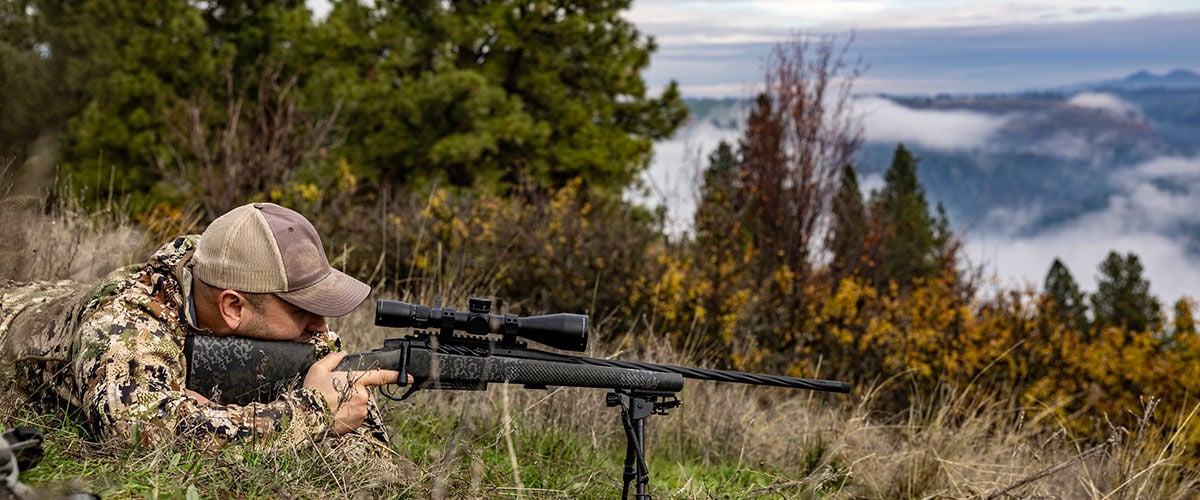 hunter in a prone position looking down rifle scope