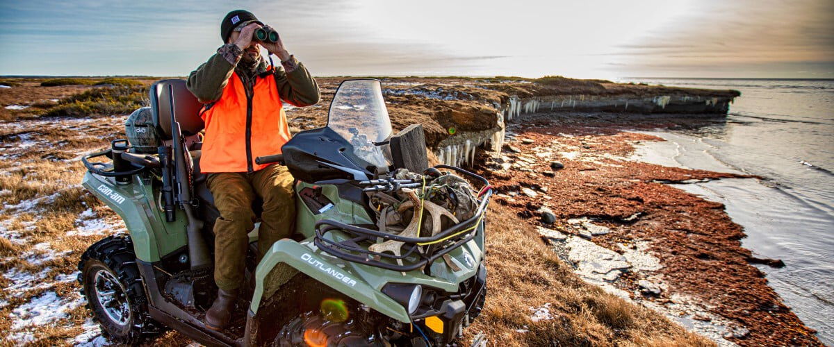 hunter sitting on a four-wheeler and looking through binoculars