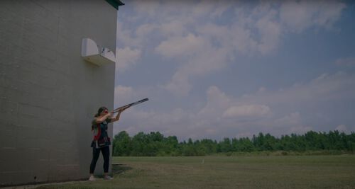 Julia Stalling standing beside a building aiming her shotgun