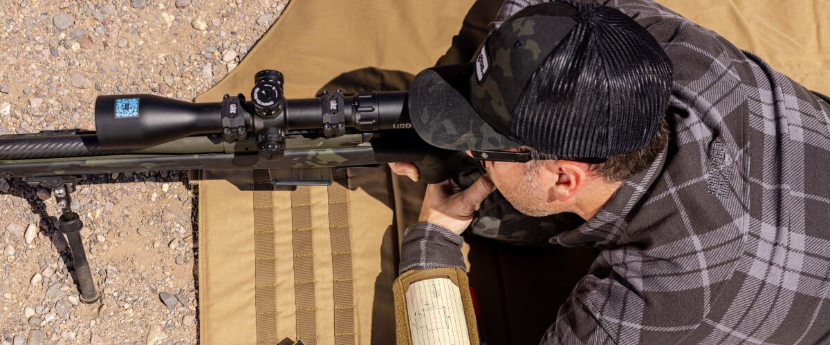 shooter laying on the ground and looking down a rifle scope