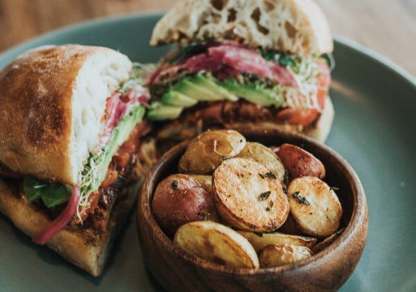 turkey sandwhich on a plate with a bowl of roasted potatoes