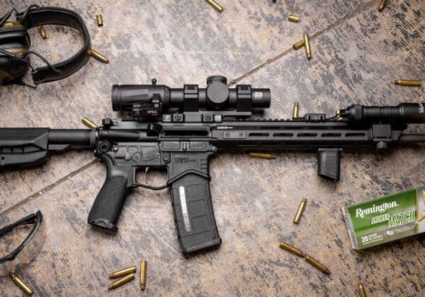 rifle laying on a table with a box of Premier Match, ear protection, and cartridges