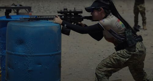 Danyela D'Angelo looking down a rifle that is rested on a blue barrel