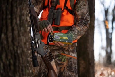 hunter removing Core-Lokt 360 Buckhammer cartridges from the box with a rifle leaning on a tree