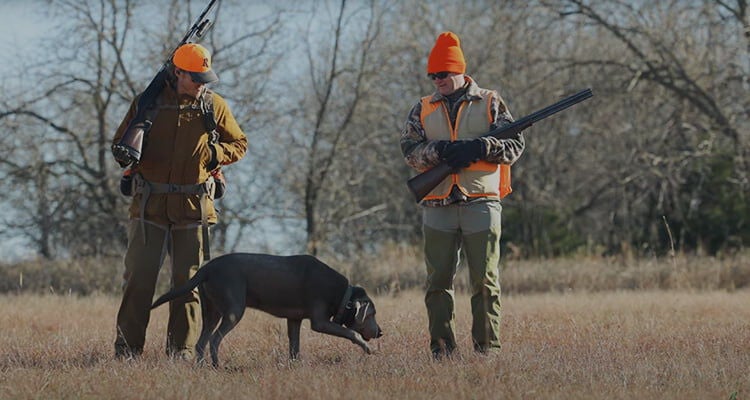 two hunters and a dog in a field