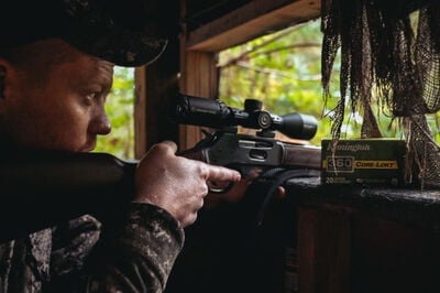 hunter looking down the scope of a rifle with a box of Core-Lokt 360 Buckhammer while in a blind