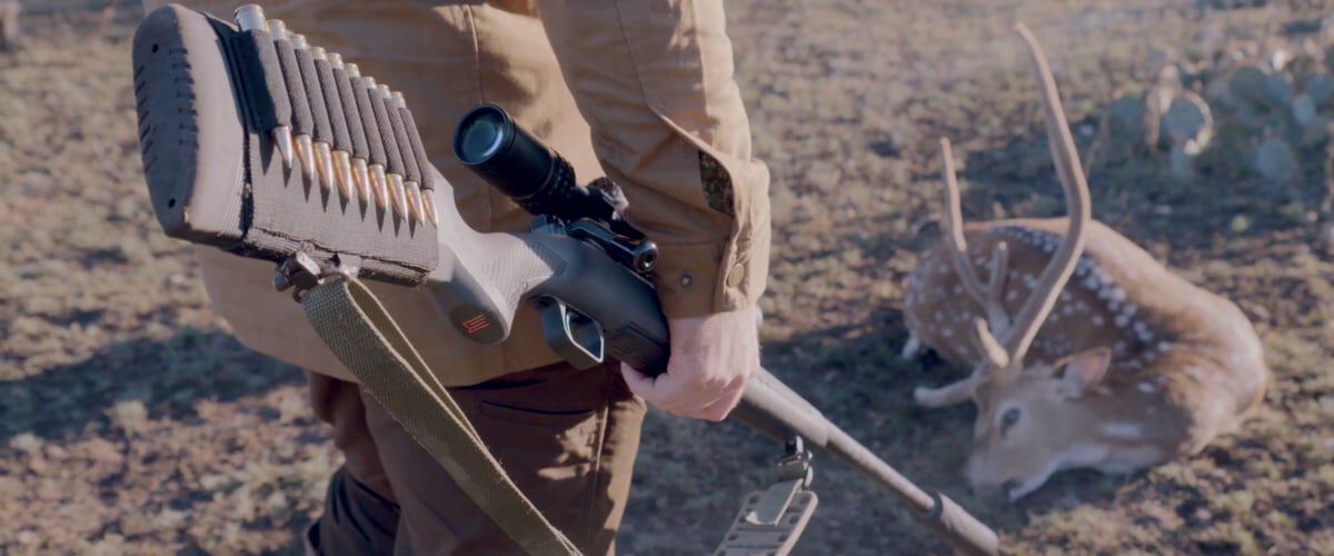 hunting holding a rifle and looking down at a dead deer