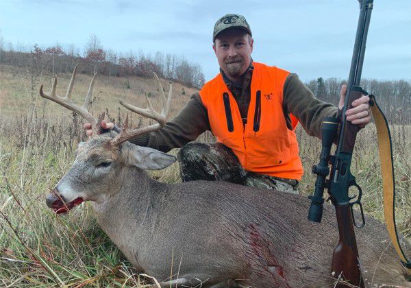 hunting holding his rifle next to a dead deer