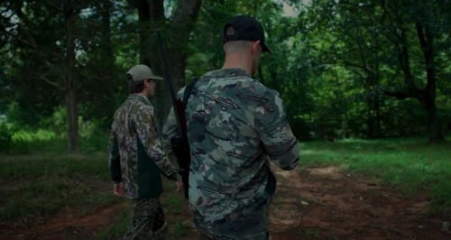 Matt Hewett walking with another hunter down a dirt road surrounded by trees