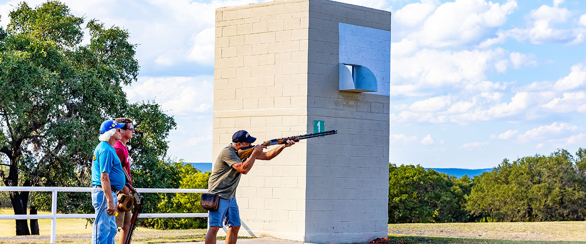 shooter aiming shotgun at skeet station
