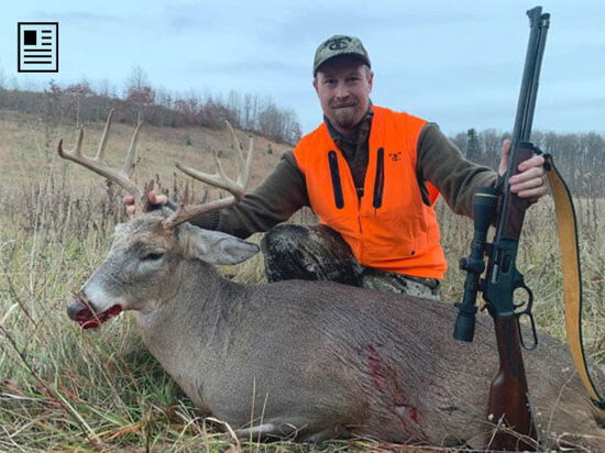 hunter holding rifle next to dead deer