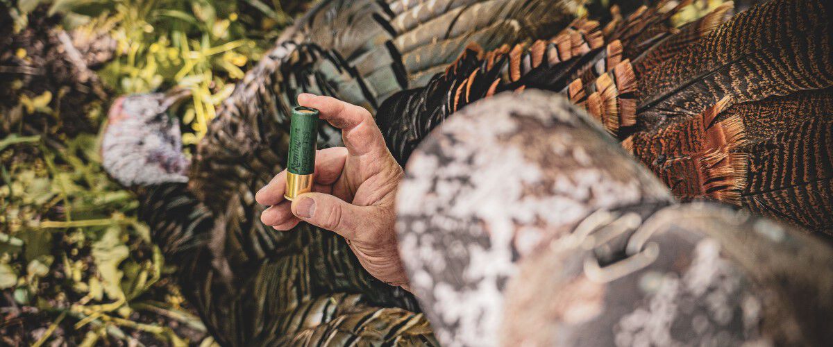 hunter holding a premier TSS shotshell in front of a dead turkey