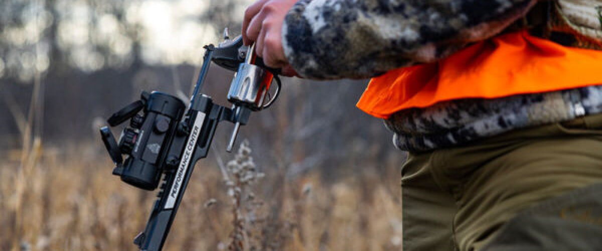 hunter loading a revolver handgun in a grassy field