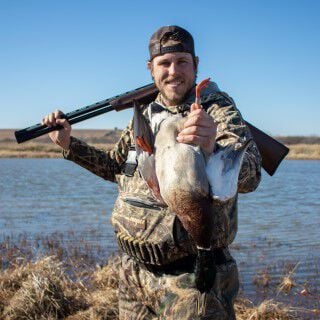 Josh Peck holding a mallard with his shotgun on his shoulder