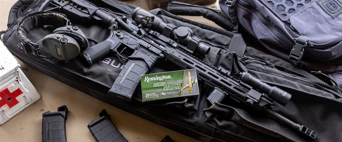 rifle on a rifle case with ear protection, magazines, and a box of Premier Match