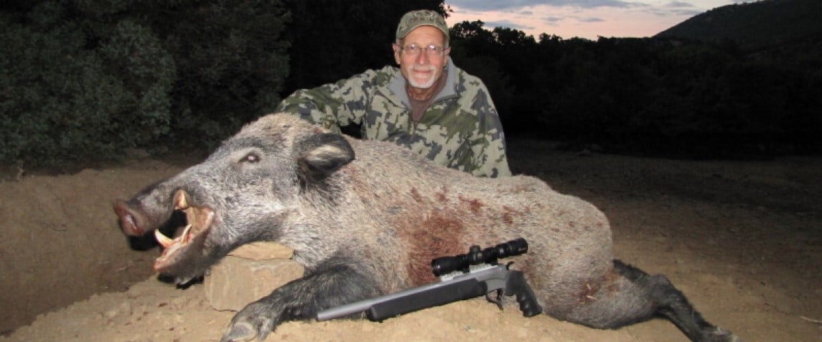 hunter sitting behind a dead hog with a hunting rifle in front