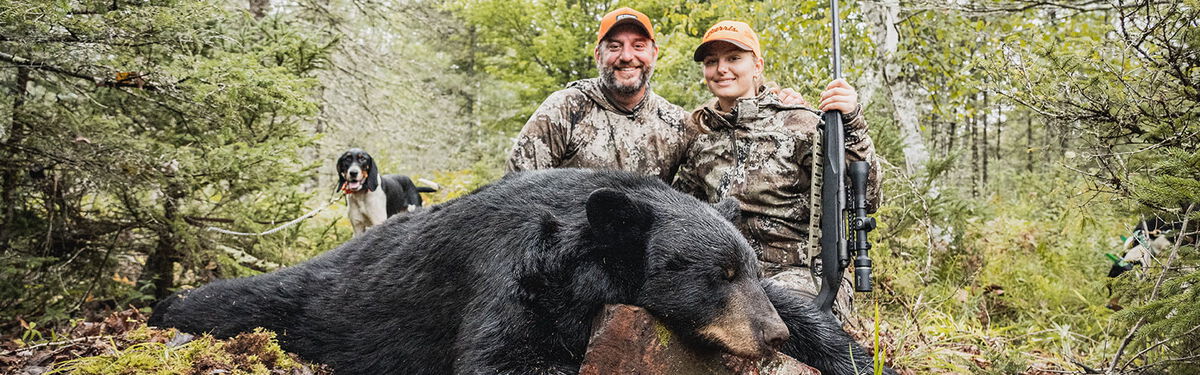 2 hunters kneeling behind a dead black bear