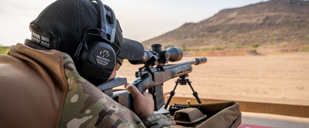 shooter looking down a rifle scope towards a hill far away