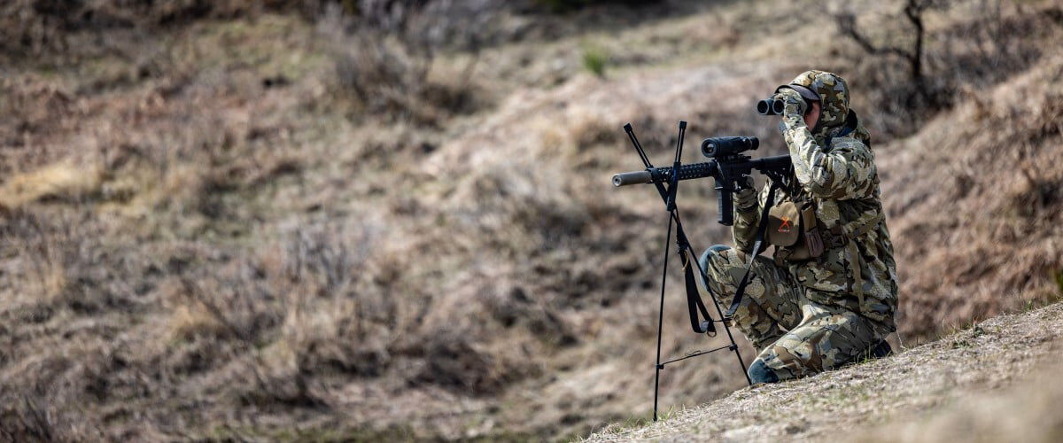 hunter looking down the scope of a rifle on a hill