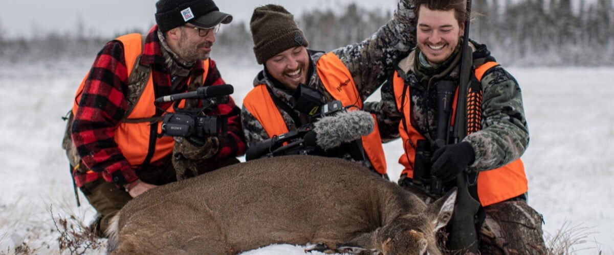 3 hunters kneeling beside a dead deer
