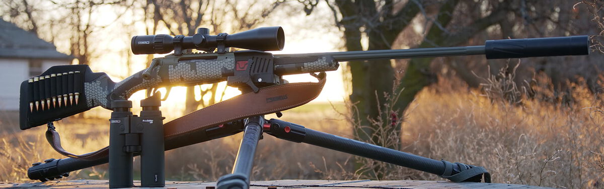 rifle on a tripod sitting outside next to binoculars