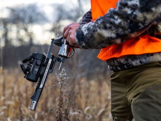 hunter loading a revolver handgun in a grassy field