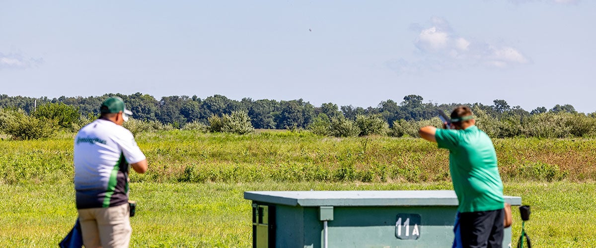shooter aiming shotshell behind a trap shooting station