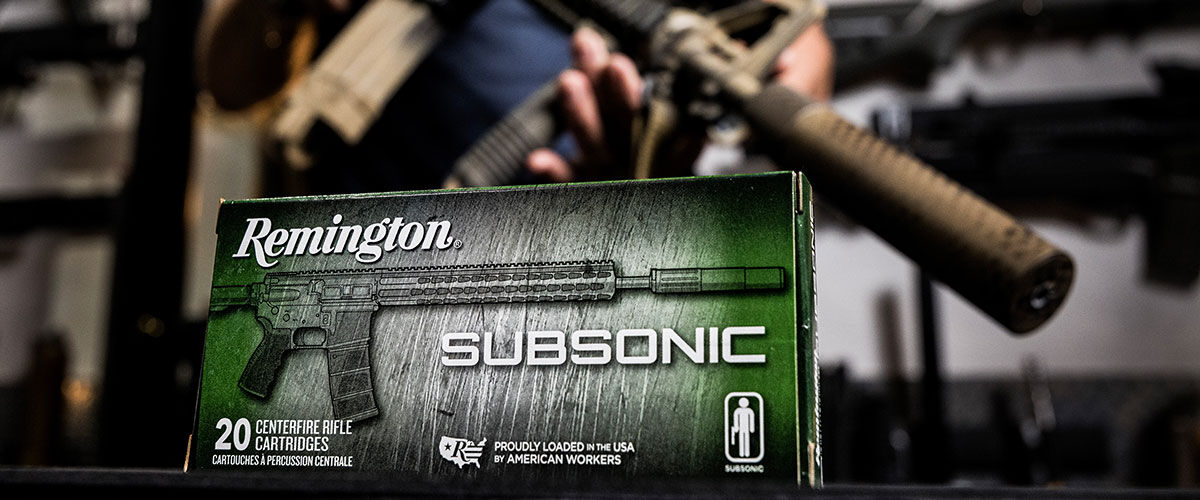 person holding a suppressed rifle behind a box of Remington Subsonic