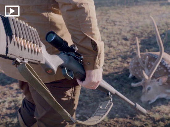 hunting holding a rifle and looking down at a dead deer