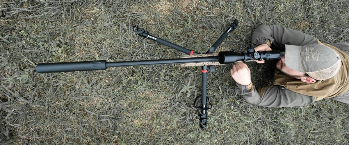 shooter looking down the scope of a rifle with a suppressor