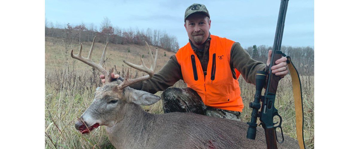 hunter holding rifle next to dead deer