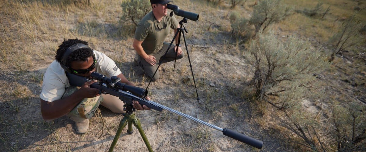 long range shooter aiming rifle with spotter next to them