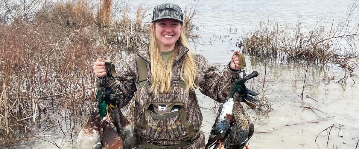 Audrey Mayes holding up ducks while standing next to a pond