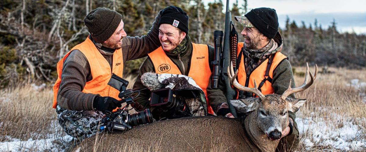 three hunters kneeling behind a dead deer and laughing
