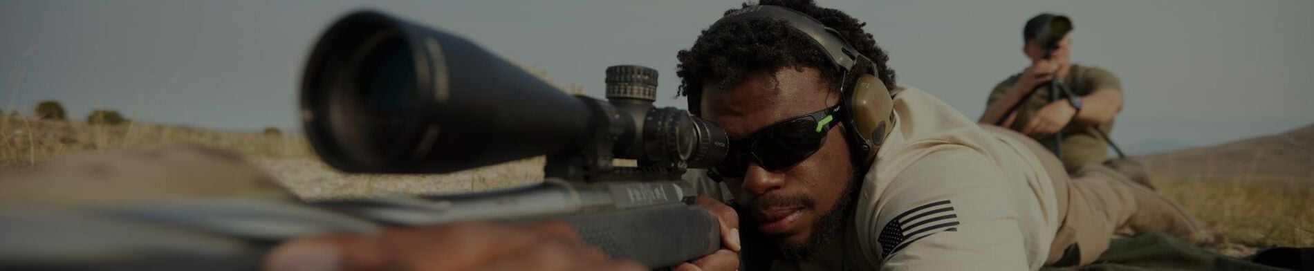 Man looking down the scope of a rifle while in a prone position