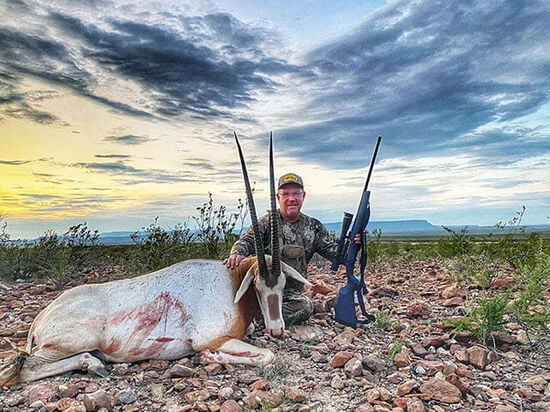 John Langenfeld kneeling beside a dead oryx