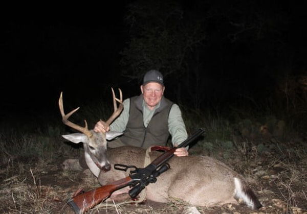 hunter kneeling down next to a dead deer